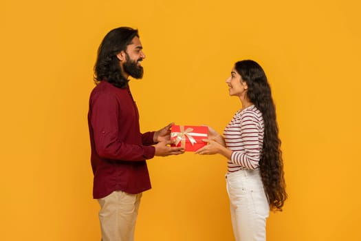 Cute young eastern couple exchanging gifts on yellow background