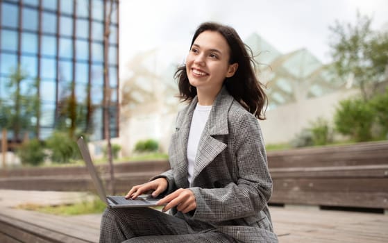 Happy business lady using laptop computer outside in urban area