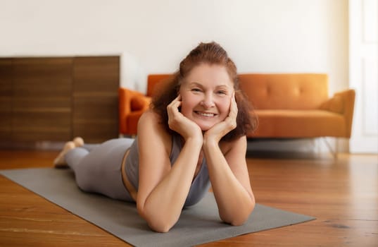 Senior woman lying on yoga mat with cheerful smile