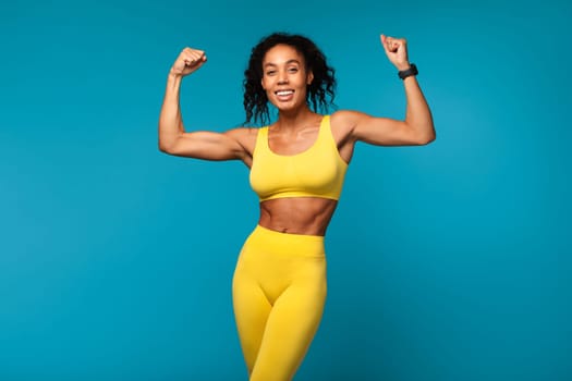 sporty black lady showing her biceps over blue studio background