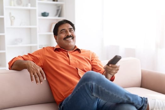 Happy mature indian man watching TV at home