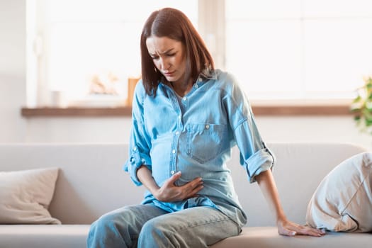 Expectant woman touches her belly in discomfort and pain indoors