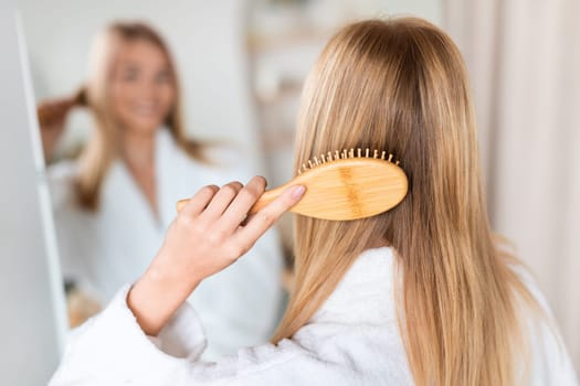 Rear view of lady combing hair near mirror in bathroom