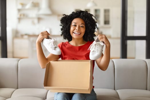 Happy young black woman unboxing parcel and holding up white sneakers