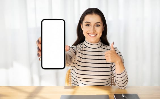 Millennial smiling arab lady show phone with blank screen, show thumb up gesture