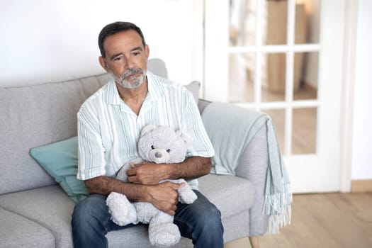 Frustrated Mature Man Holds Fluffy Bear Toy Sitting Depressed Indoors