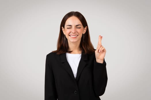 Cheerful young European woman in suit crossed her fingers and make a wish sign