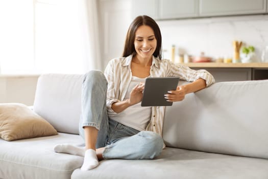 Young woman browsing internet on digital tablet while relaxing in living room