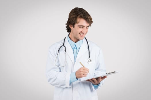 Focused male doctor writing on clipboard with a pen
