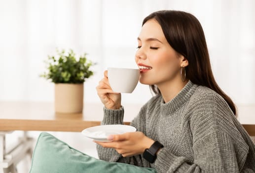 Closeup of happy young woman drinking coffee at home