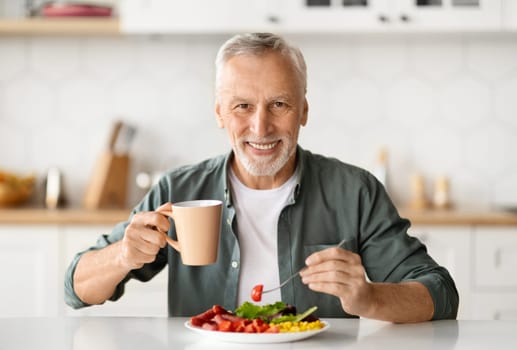Smiling elderly man eating lunch and enjoying cup of coffee