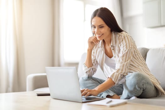 Smiling young woman using laptop for remote work at home