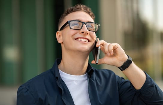 A young man with glasses smiling while talking on a smartphone
