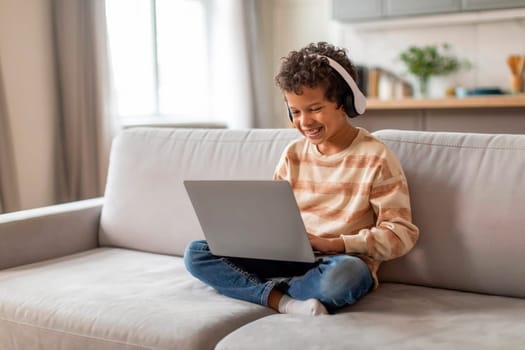 Little black boy wearing headphones using laptop computer at home