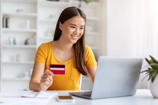 Smiling Asian Female Freelancer Using Laptop And Credit Card In Home Office