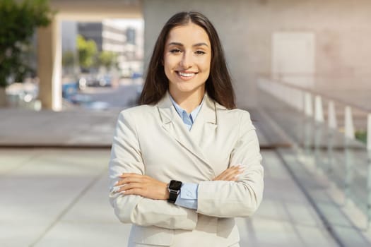 Confident european millennial businesswoman with crossed arms smiling in urban setting