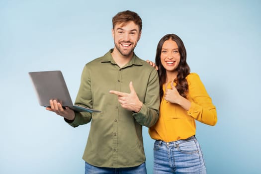 Couple with laptop pointing at computer on blue background
