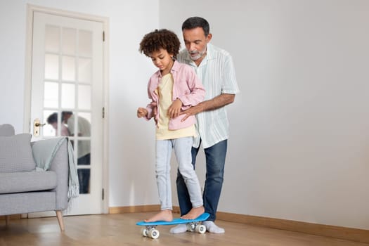 Mature Grandpa Teaching His Grandchild To Ride Skateboard At Home
