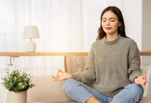 Peaceful young woman sitting on couch in lotus position