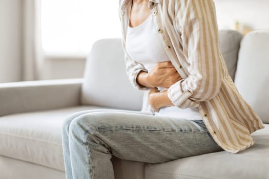Uncomfortable young woman holding her abdomen, feeling unwell with stomach ache