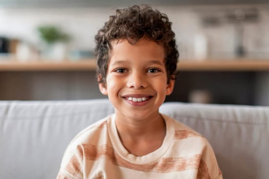 Cheerful black boy with curly hair and bright smile looking at camera