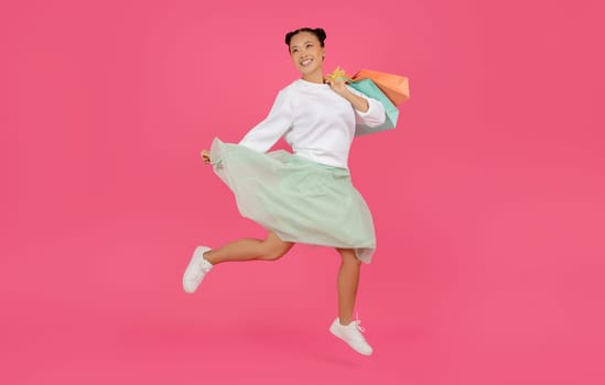 Happy asian woman jumping high with shopping bags in her hands