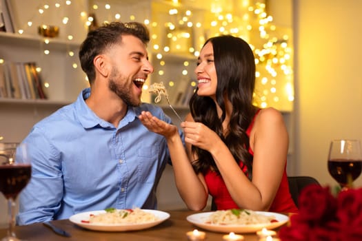 Couple sharing a playful moment with pasta during romantic dinner