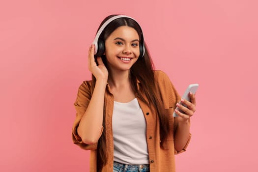 Smiling teenage girl enjoying music on her headphones while holding smartphone