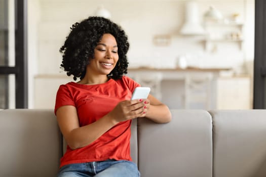 Young happy black woman texting on her phone at home