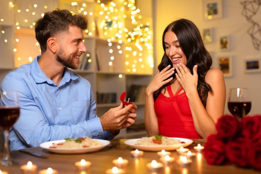 Man proposing with ring, delighted woman at dinner