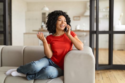 Cheerful young black woman speaking on mobile phone at home