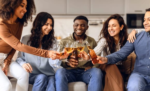 Group of multiethnic friends clinking beer glasses and bottles indoor