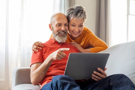 Cheerful Senior Spouses Browsing Internet On Laptop While Relaxing At Home