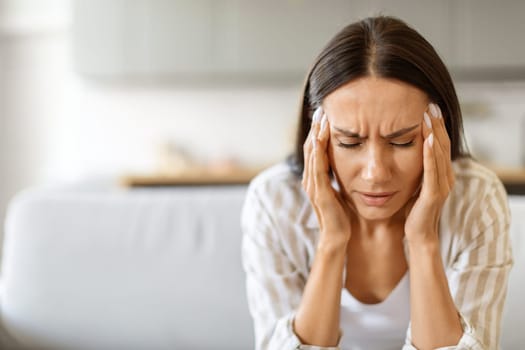 Woman in distress with severe headache, pressing her temples and frowning