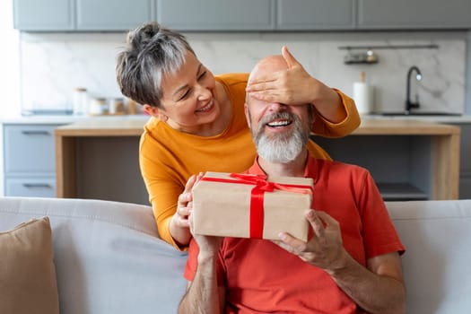 Wife Surprising Senior Husband With Present, Covering His Eyes And Giving Gift