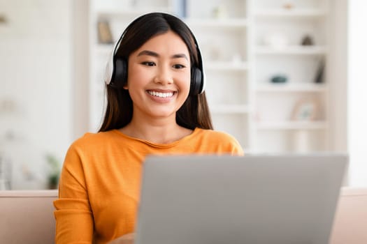 Closeup of smiling asian woman using laptop and headphones