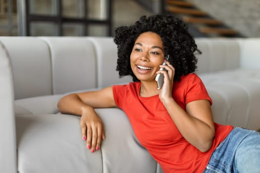 Cheerful young black woman chatting on her smartphone while relaxing at home