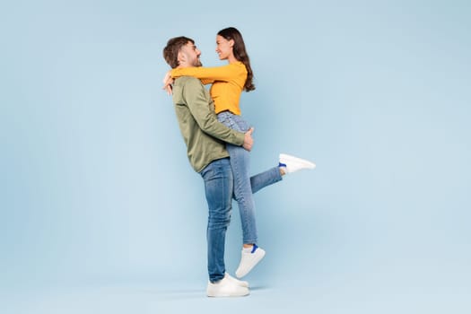 Man lifting woman in joyful hug on blue backdrop, full length