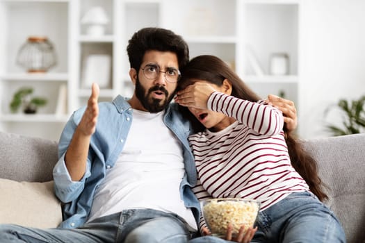 Scared millennial indian couple watching movie together at home