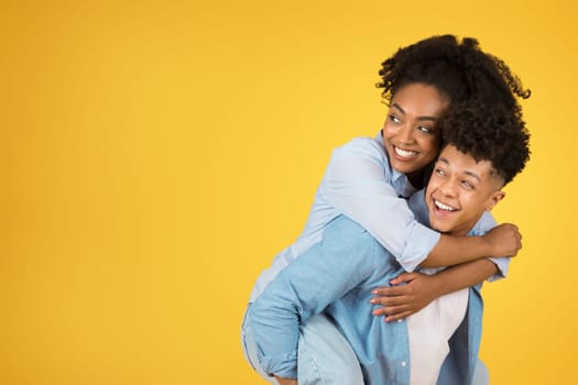 Happy young african american guy holding woman on his back, have fun, looking at empty space
