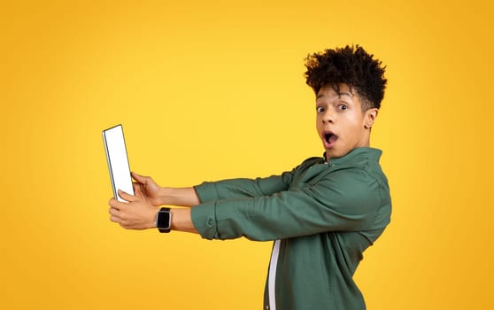 Amazed young black guy holding digital tablet with blank screen