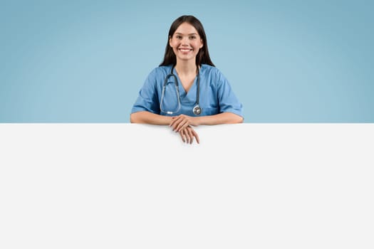 Smiling nurse in blue leaning on blank space placard