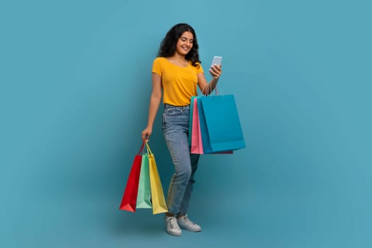 Positive young indian woman with purchases and smartphone