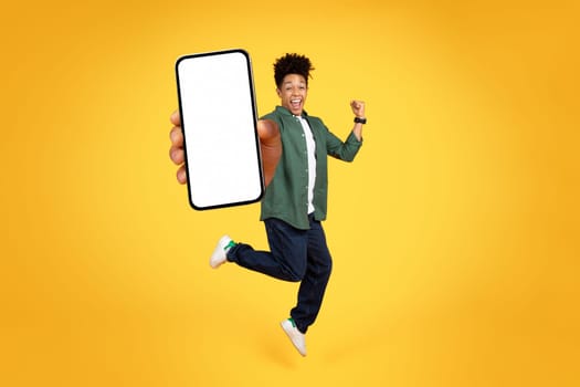 Joyful young black guy jumping with phone in his hand