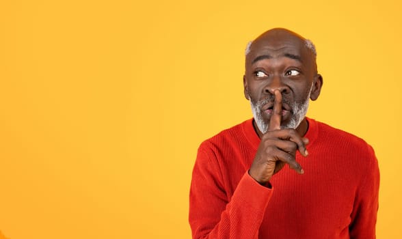 Secretive senior Black man with a white beard placing a finger to his lips in a shushing gesture
