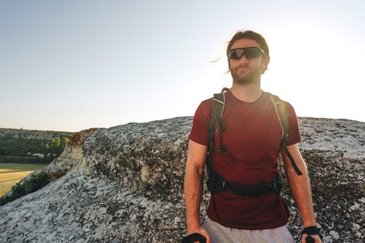Bearded traveler with a backpack and sunglasses on the top of a mountain