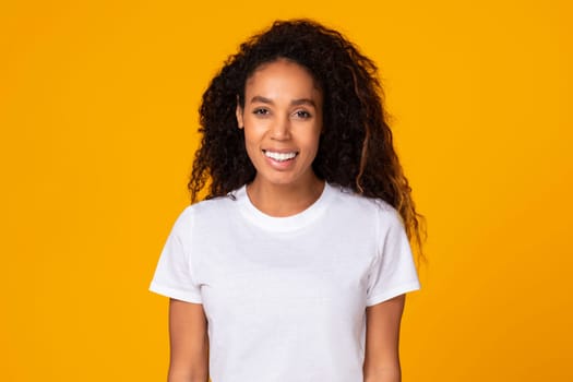 Black young lady with curly hair expressing positivity, yellow background