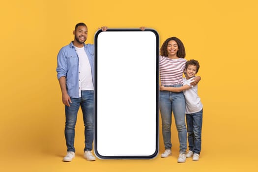 Happy Black Family Standing Near Big Smartphone With Blank Screen