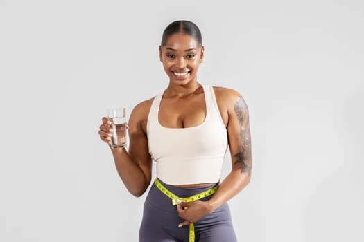 Sporty black lady examining fitness results with measure tape, studio