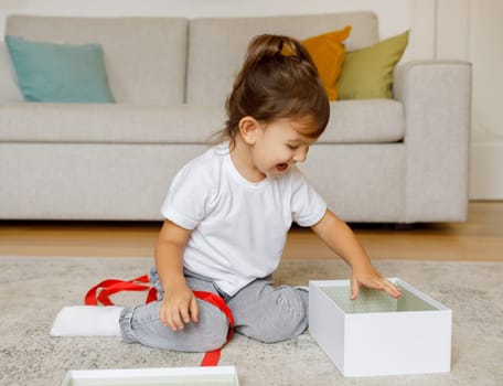 Joyful little girl opening gift box at home